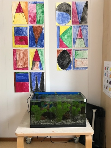 Bild på akvarium med fiskar och på väggen hänger målningar som barnen har gjort